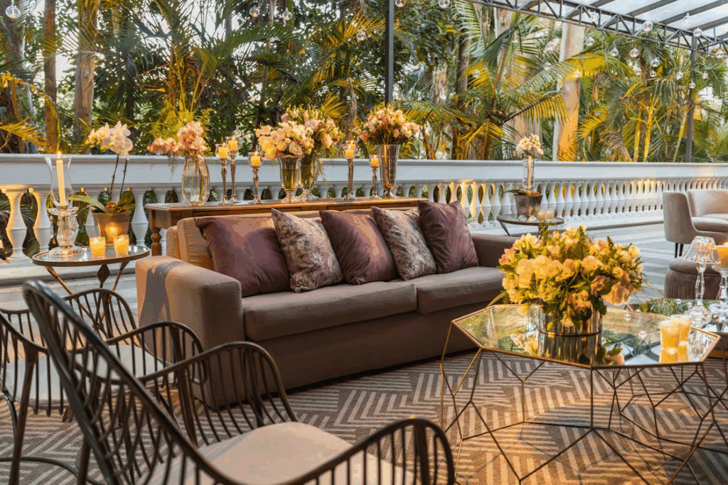 Outdoor living room ideas with a cozy sofa, throw pillows, candles, and flowers styled to feel like an indoor space on a patio