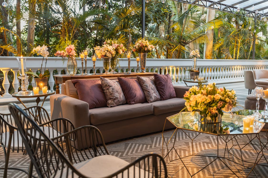 Outdoor living room ideas with a cozy sofa, throw pillows, candles, and flowers styled to feel like an indoor space on a patio