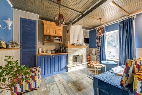 Eclectic living space mixing vintage and modern with bold blue cabinets, retro patterned chairs, and rustic wood ceiling.