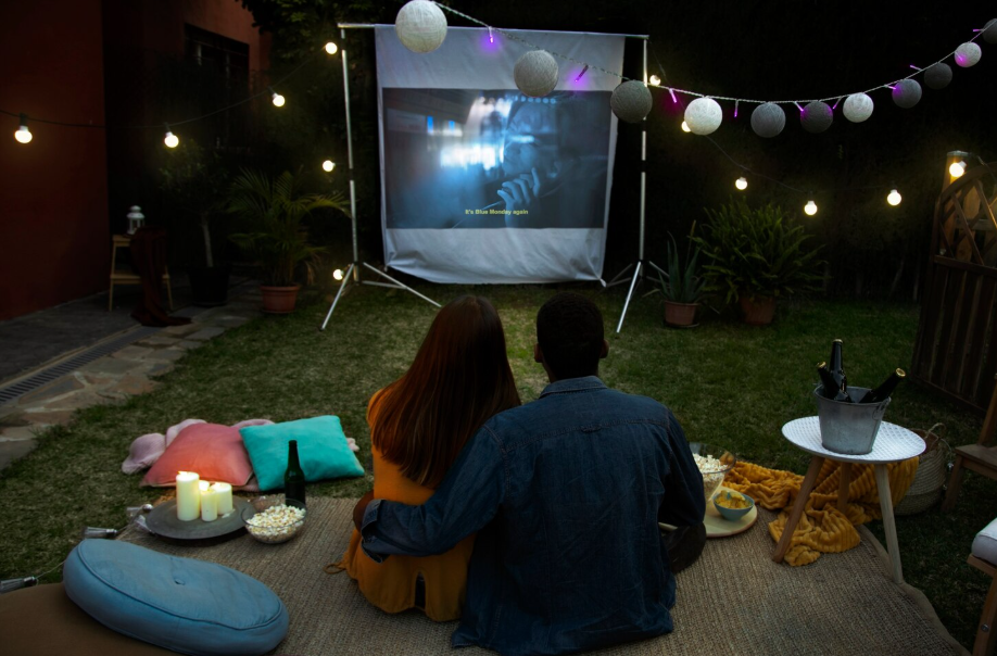 Backyard outdoor movie night with screen, pillows, popcorn, and string lights