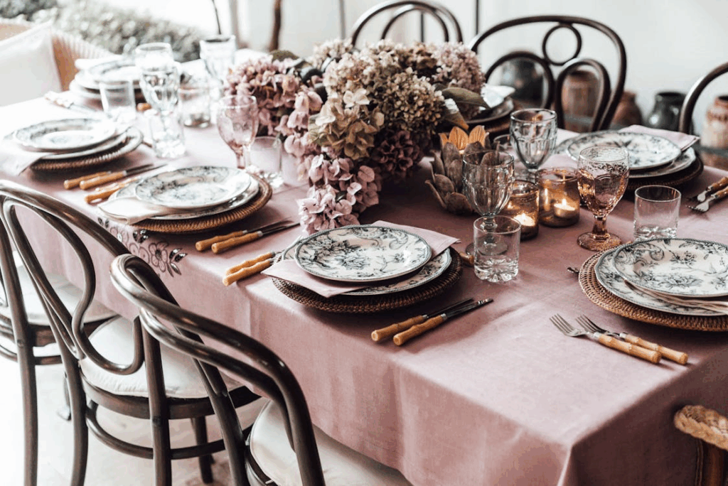 Elegant seasonal table setting with floral centerpiece, layered plates, linen tablecloth, and candles