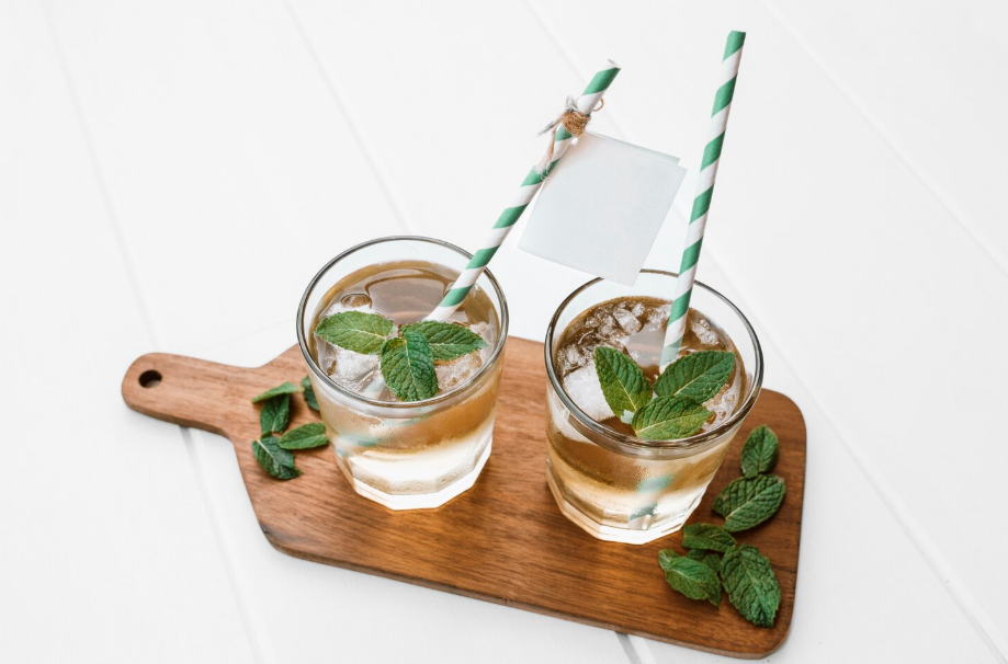 Two herb cocktails with mint leaves served on a wooden board with striped straws.