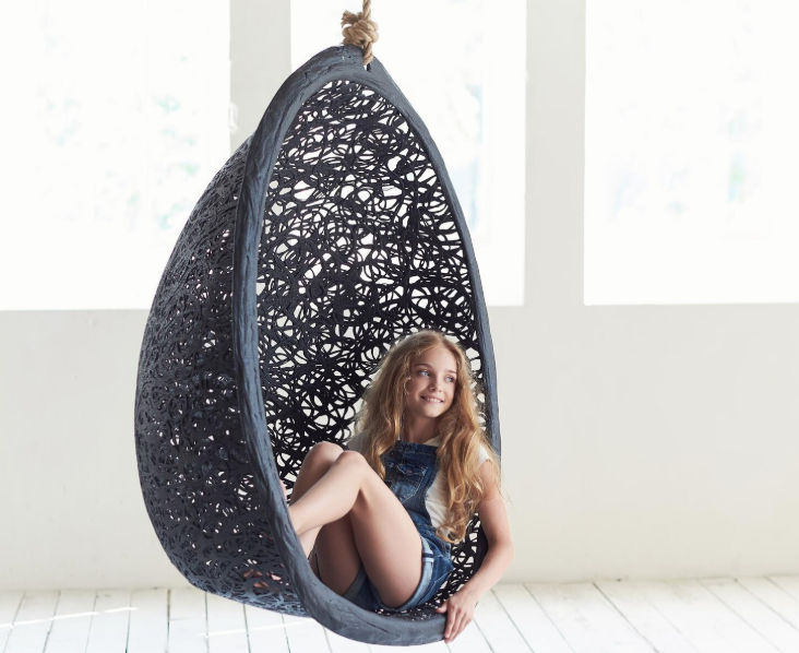 Stylish black hanging egg chair with girl sitting comfortably, modern indoor furniture idea