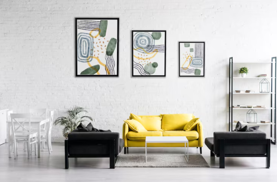 Modern living room with a yellow sofa and three abstract framed prints arranged in a clean grid gallery wall layout.
